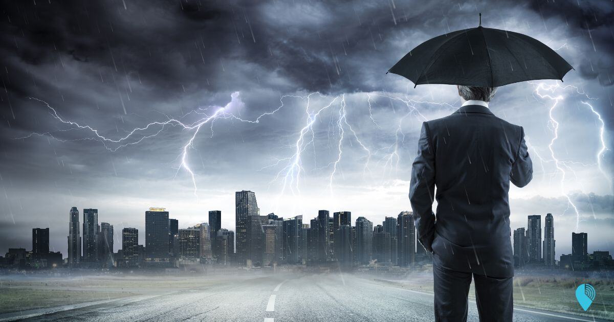 Business man standing under umbrella looking at the storm in city